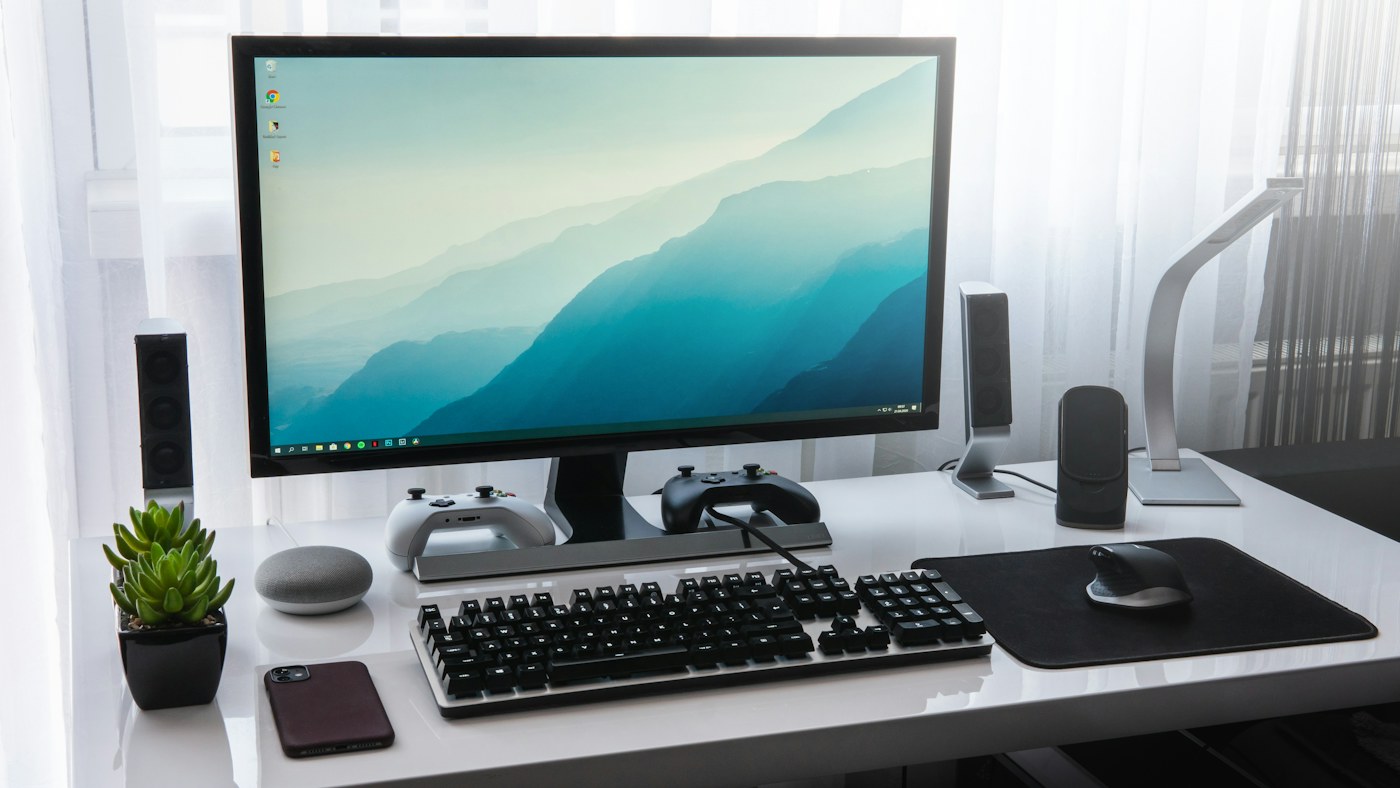 A computer monitor, keyboard, and game controllers on a white desk in a workspace. Illustrative photograph; not a depiction of the named product or organisation.